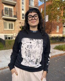 A photo of shirt model Marcela Huerta wearing a Metatron x Metonymy Shirt designed by Janes Harmes. Marcela is wearing a Black shirt with a design printed in white ink.